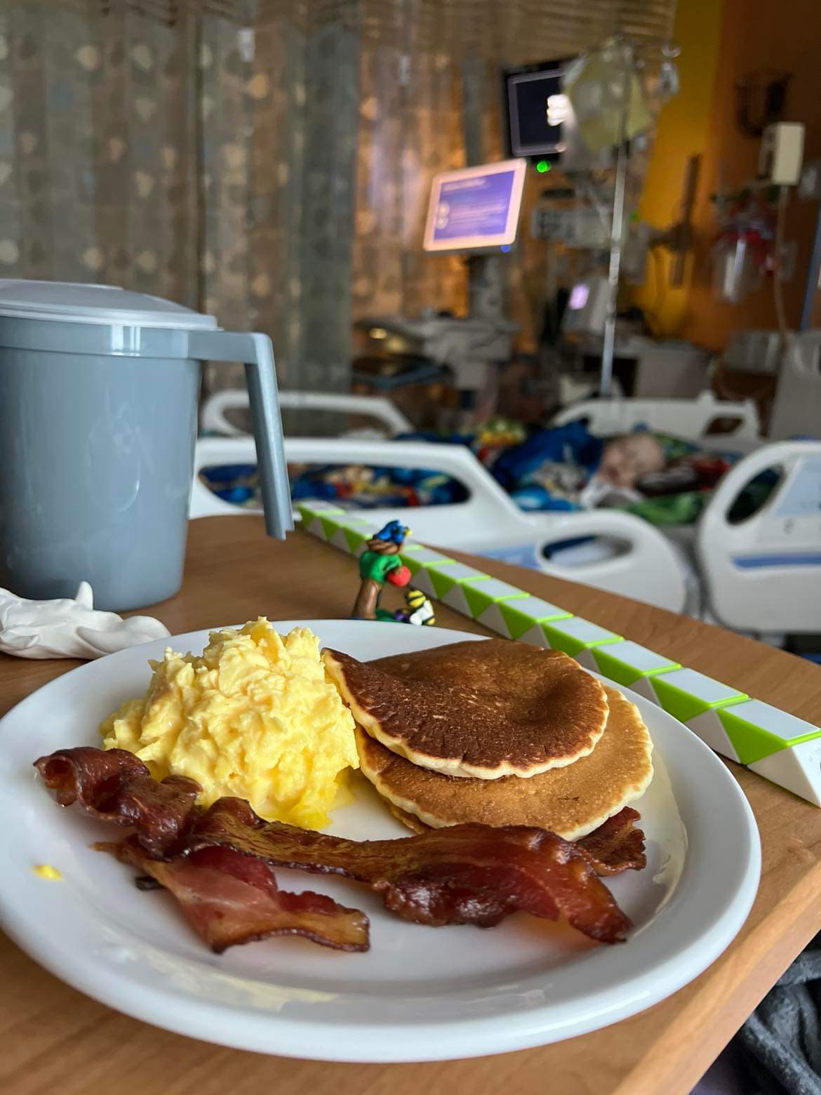 Parent meal in focus and child in hospital bed just out of focus.